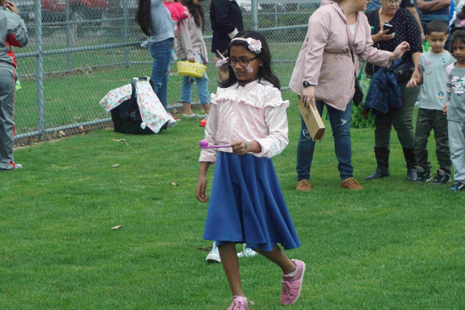 A girl wearing glasses, pink top, and a blue skirt, walking