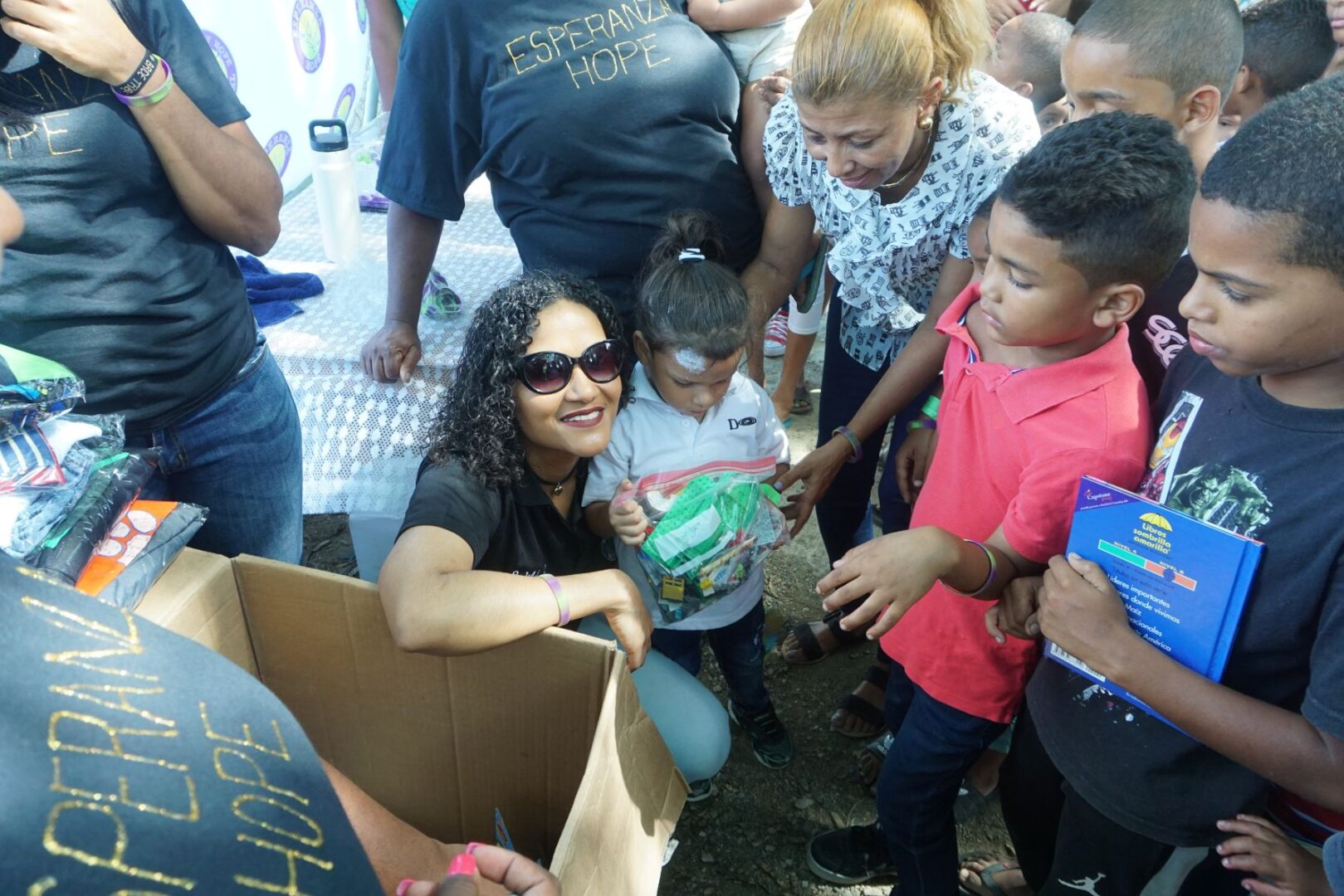 A female staff and a young child holding a plastic bag and surrounded by a crowd of parents and children