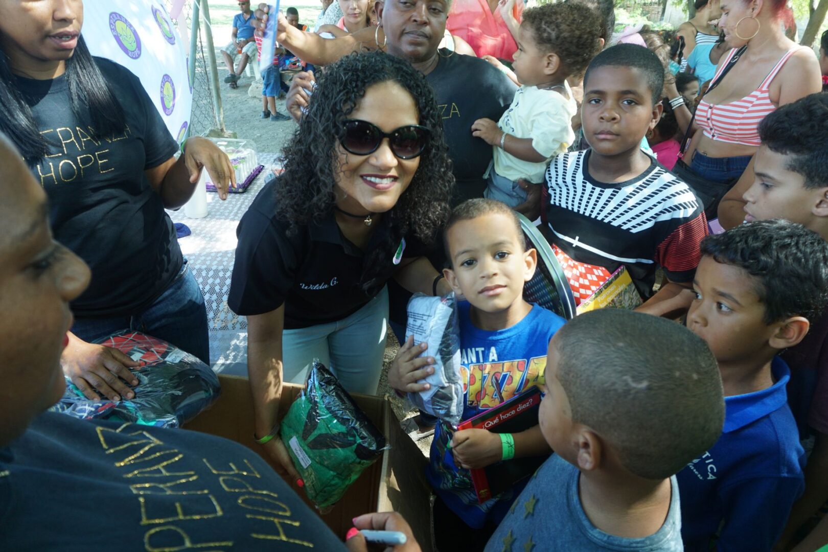 A female staff and a boy holding a book and a plastic of clothes, smiling, and surrounded by crowd
