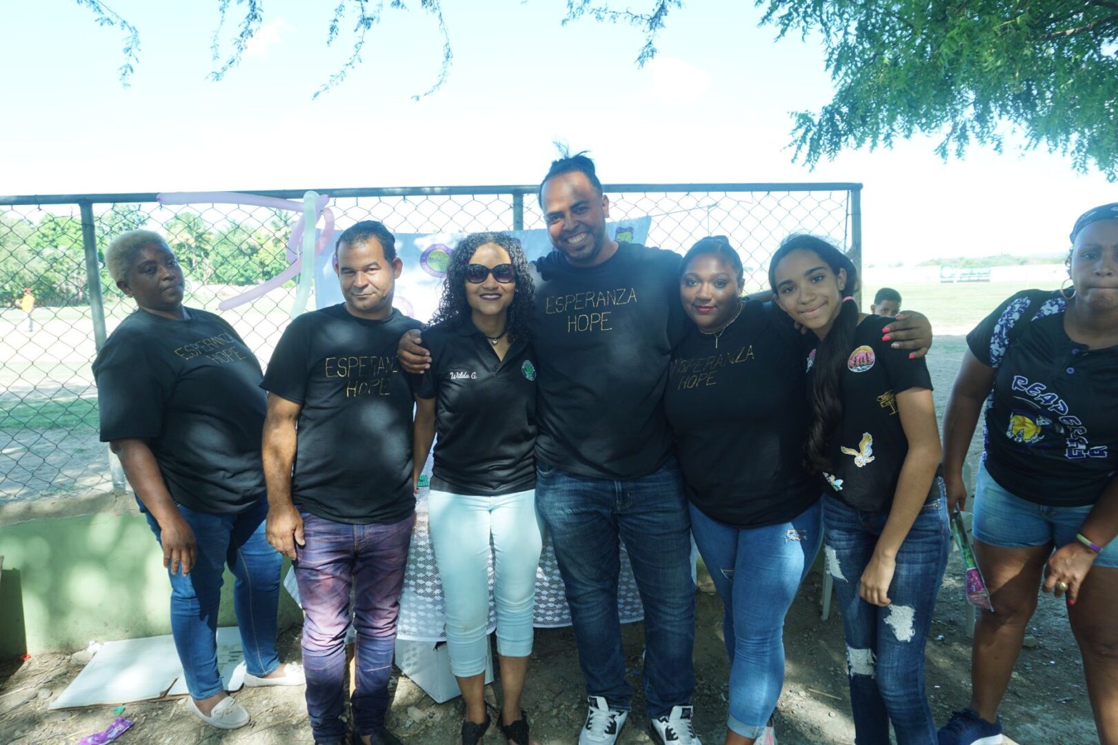 Two men and six women, all wearing black shirts and having their arms around each other