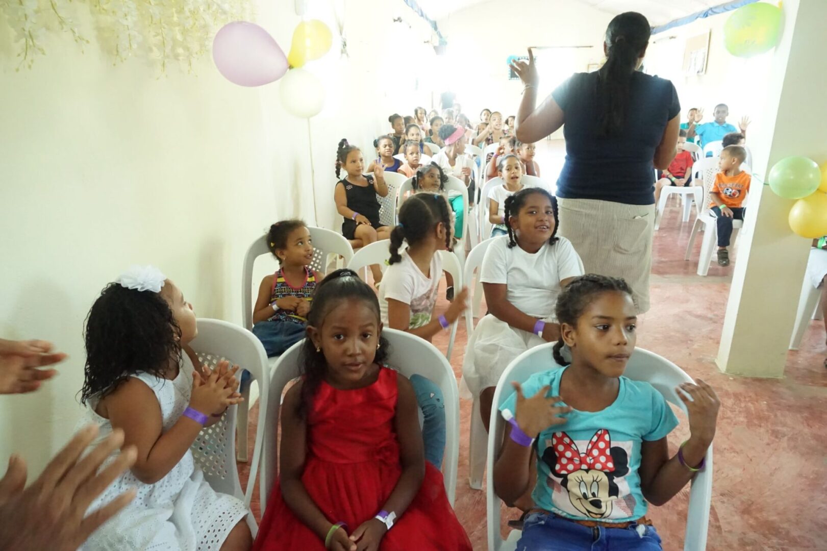 Girls sitting in white chairs clapping and singing