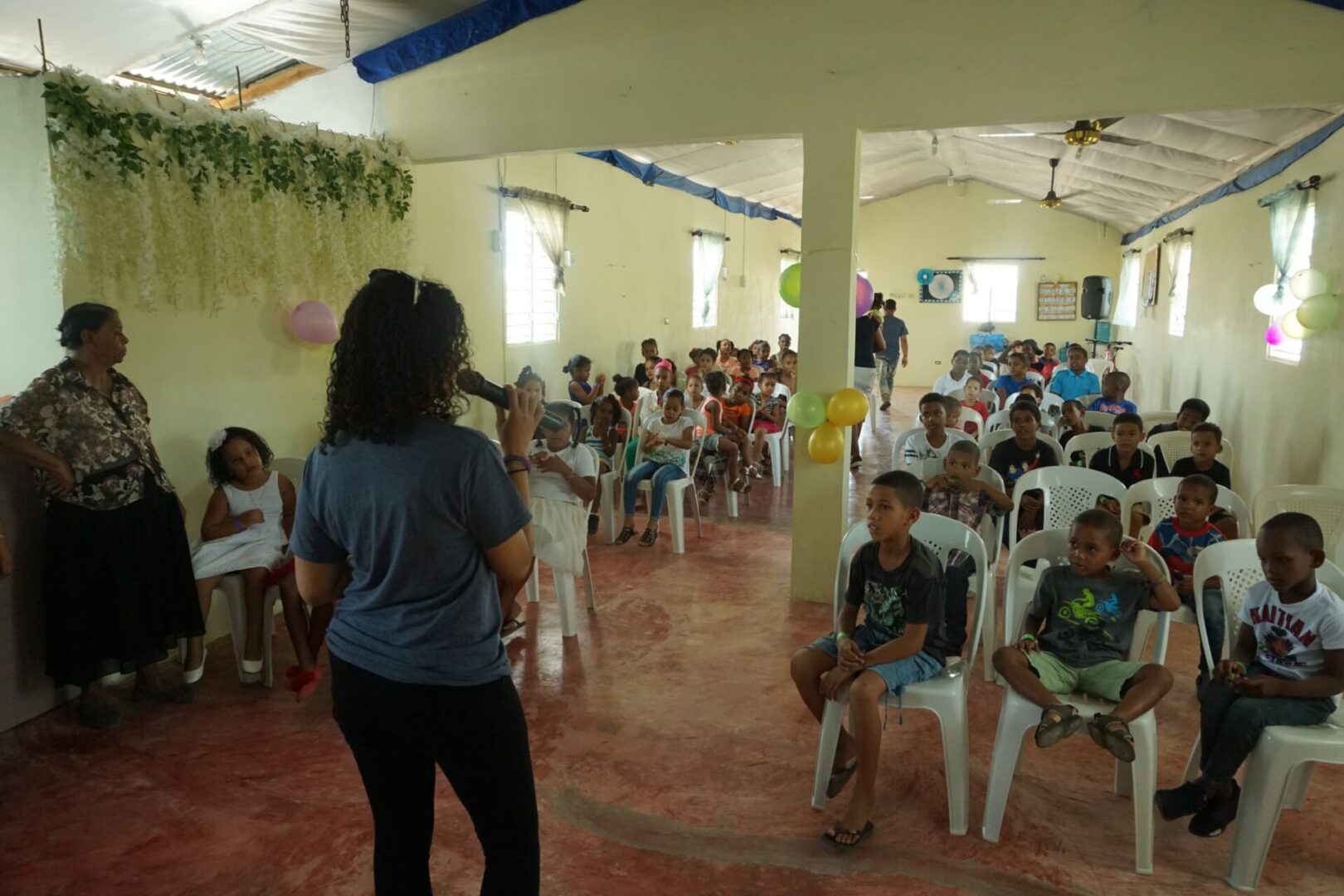 A woman talking into a mic in front of the children in the church