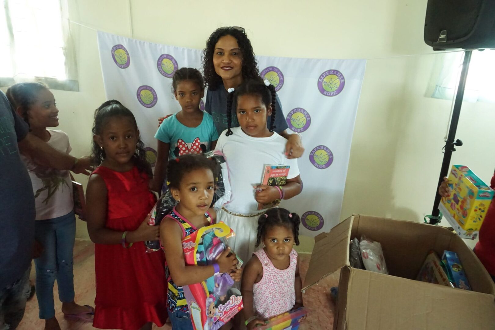 A female staff and a group of girls with toys; Esperanza-Hope logo in the cloth at the back