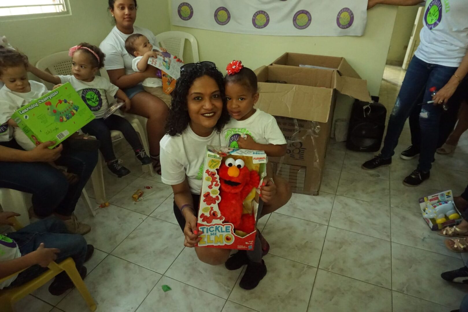 A female staff holding an Elmo toy with her arms around a little girl, smiling