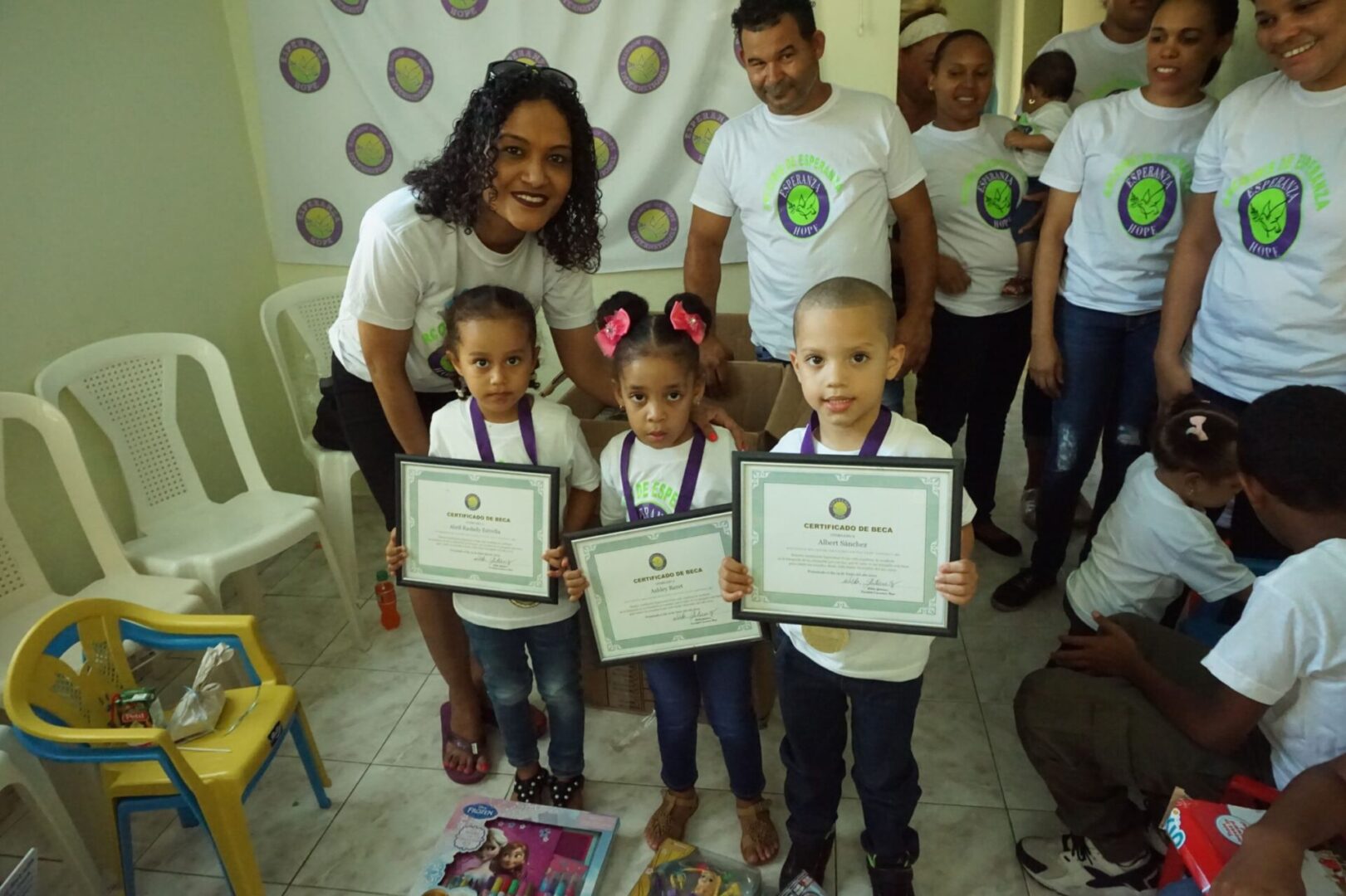 Two little girls and a little boy wearing their medals and showing their certificates, smiling