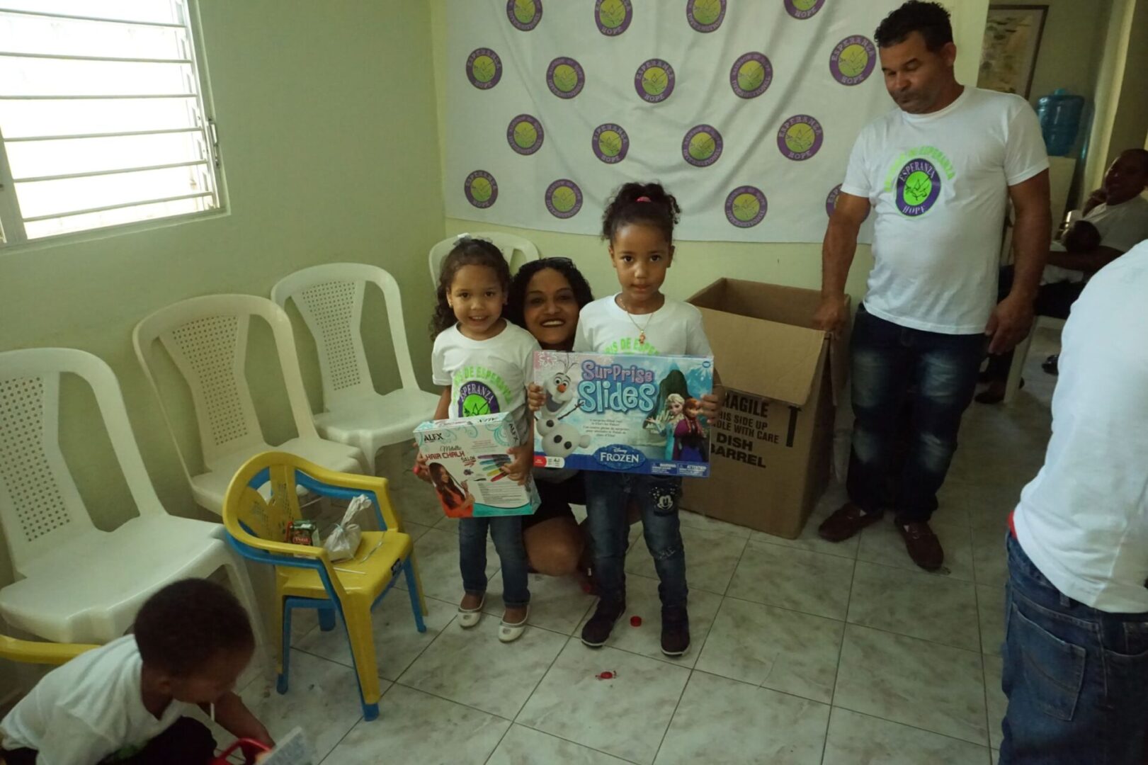 A female staff together with two little girls smiling and holding their boxes of toys