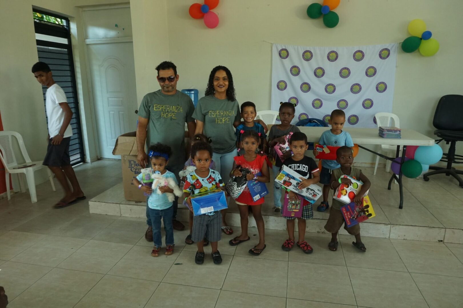 A male and female staff together with the group of young girls and boys who received toys