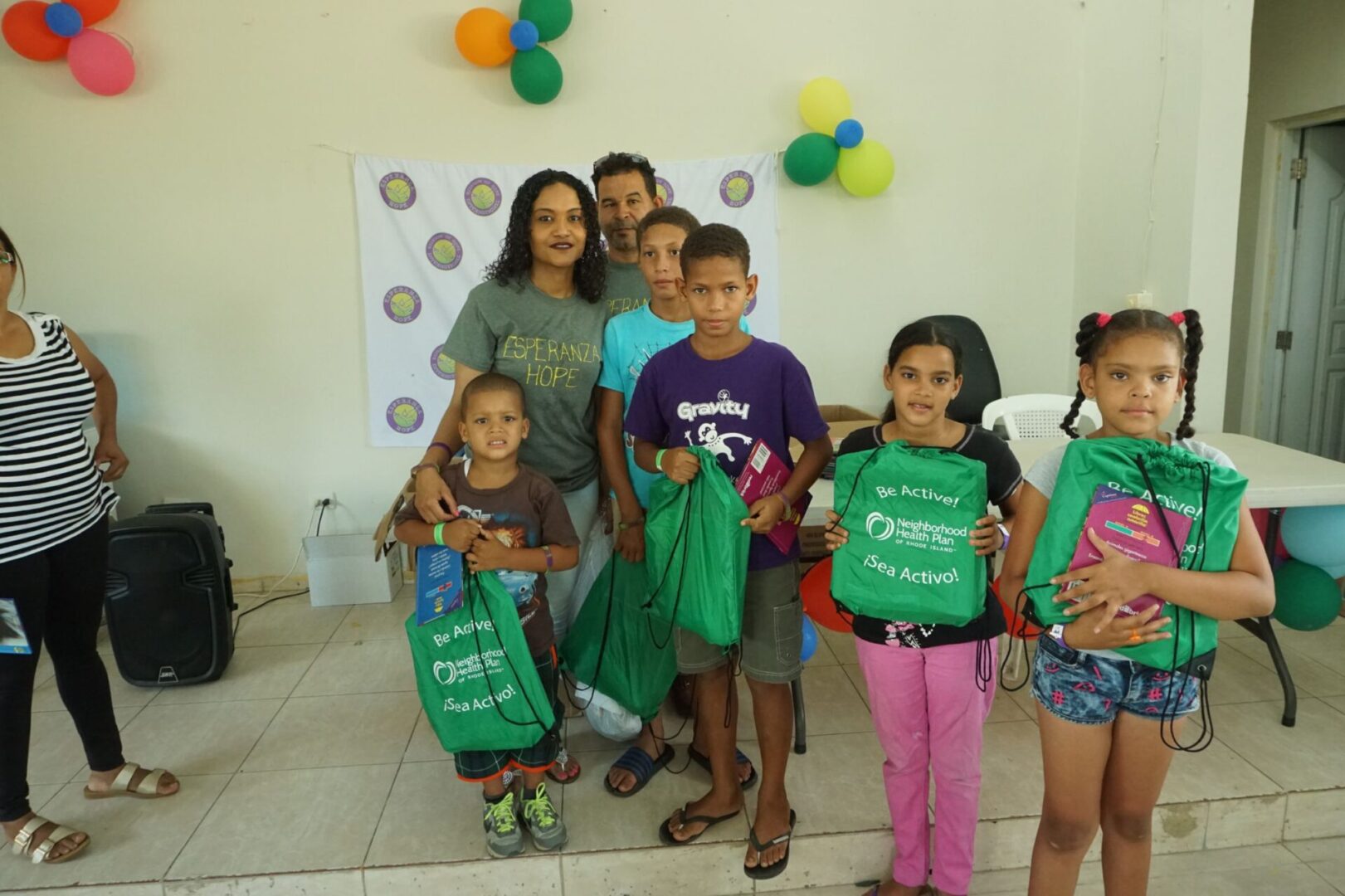 Two staff and a group of children holding a green string bag