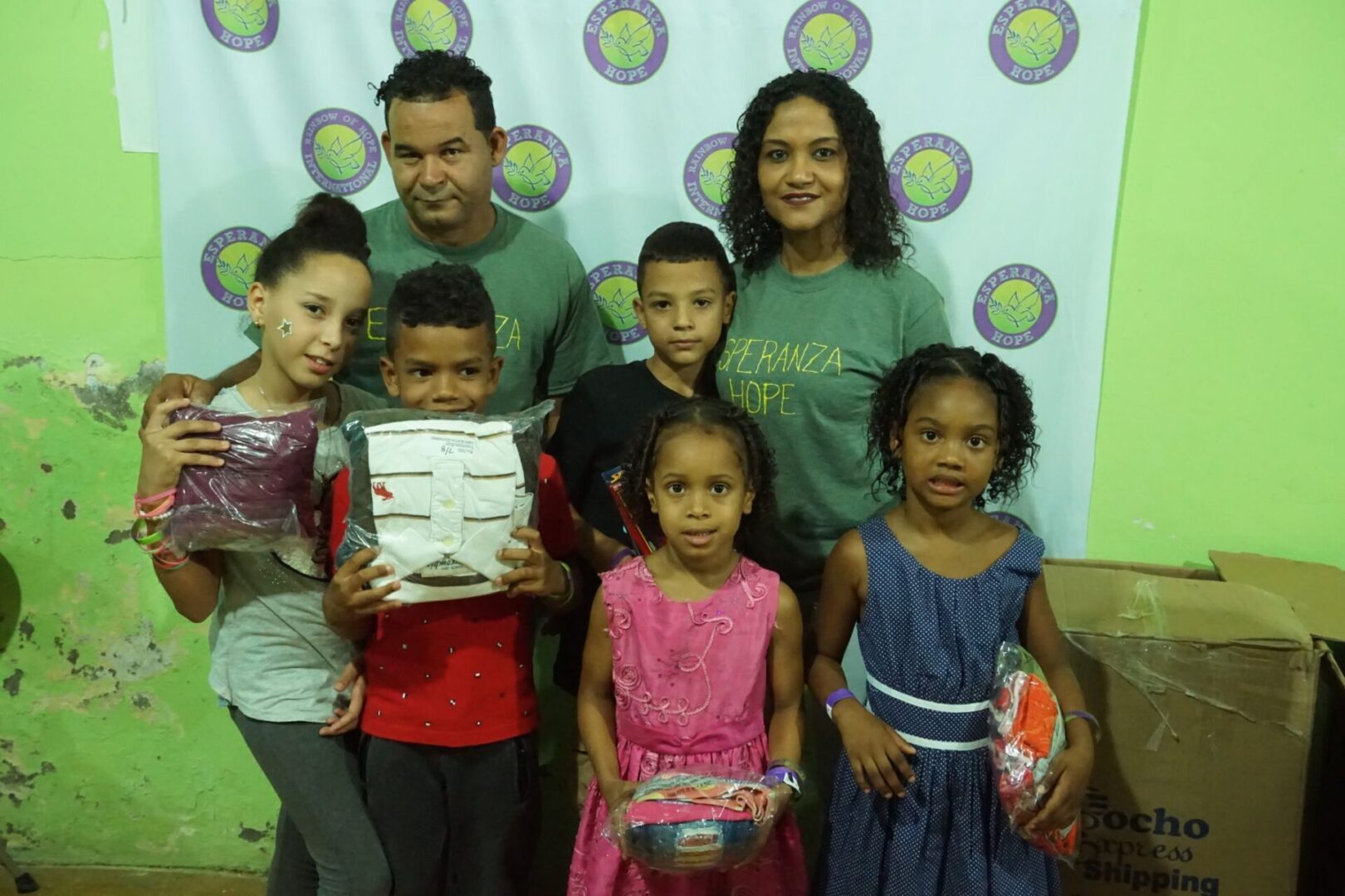 Two staff and a group of children holding toys, standing against a cloth with our logo