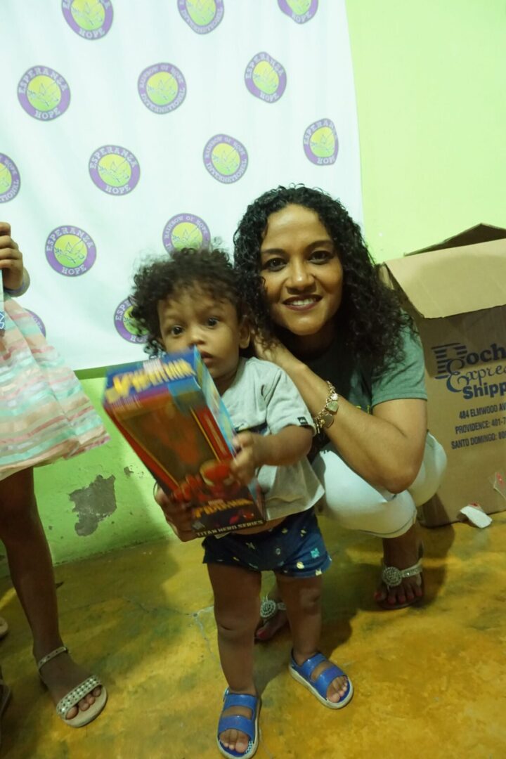 A staff crouching down to a little girl shaking a box of toy