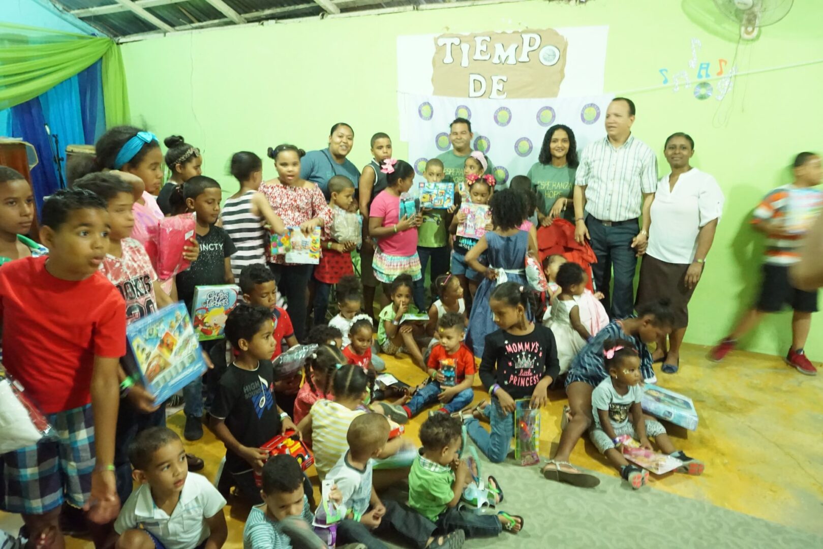 All of the children and the staff gathers in front of the room with their toys (bright), 3