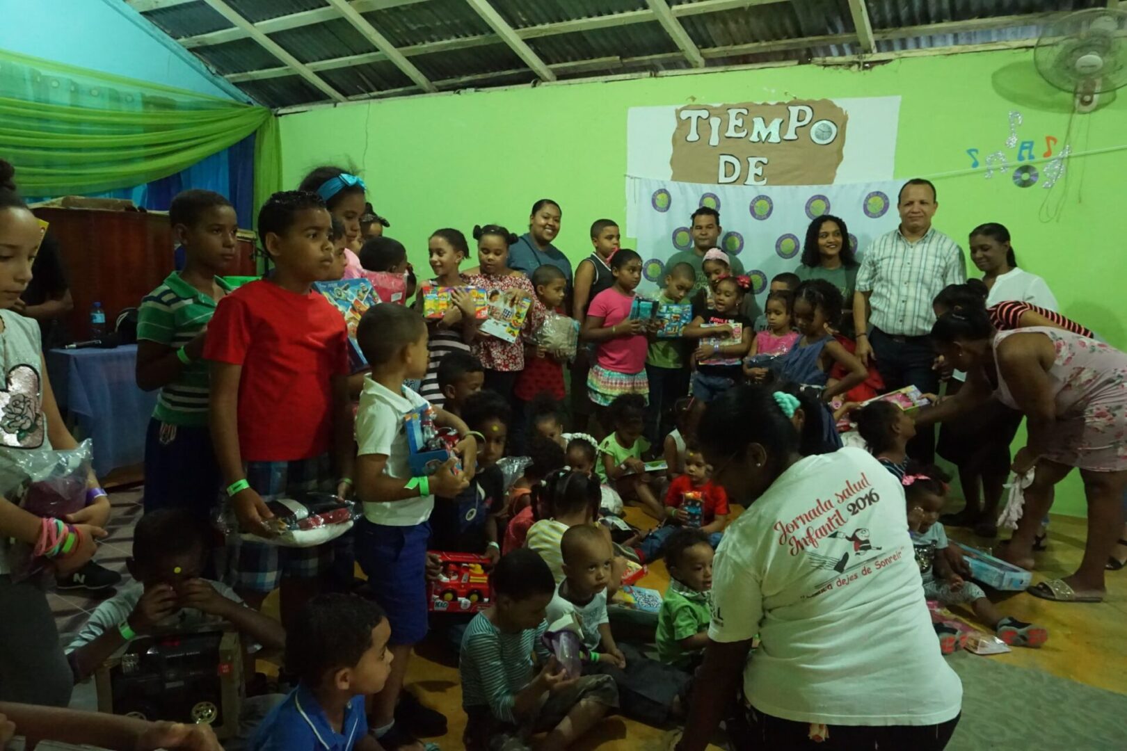 All of the children and the staff gathers in front of the room with their toy; several parents go to the children