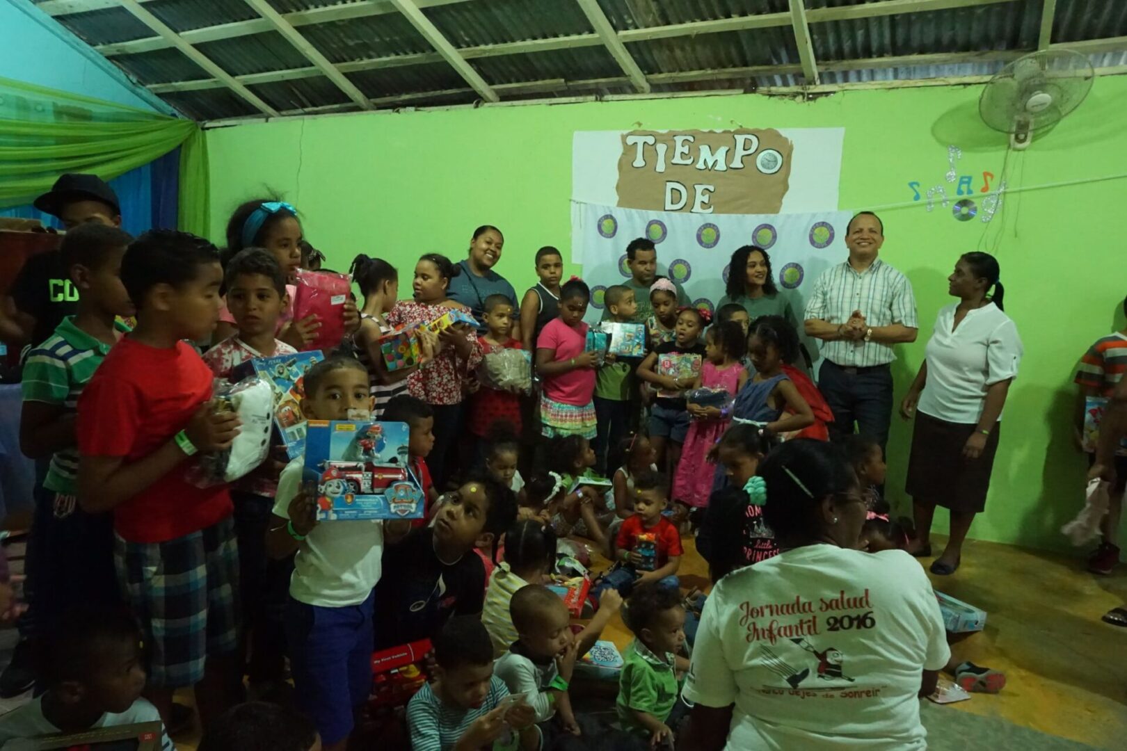 All of the children and the staff gathers in front of the room with their toy, with some of the children on the floor