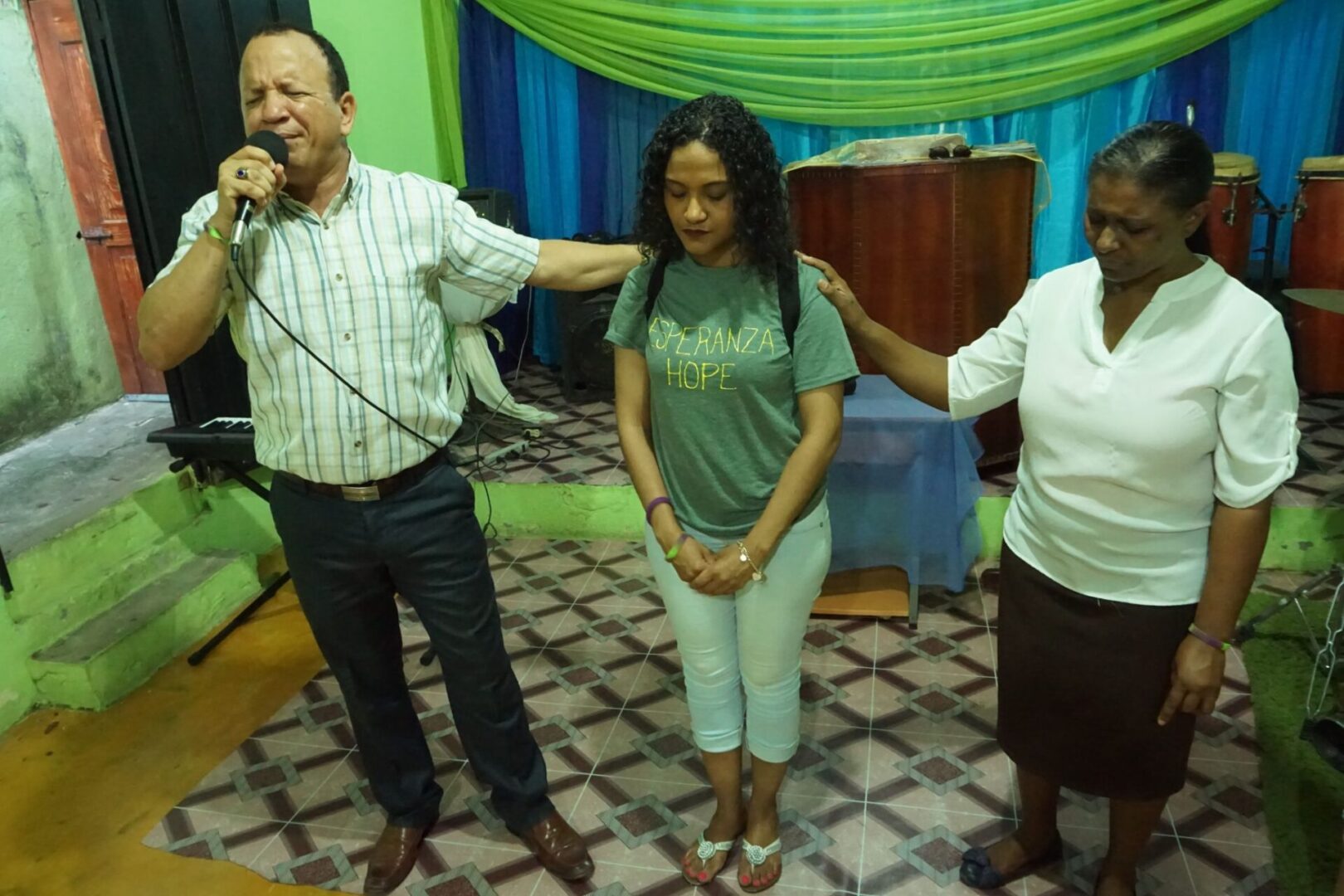 A man speaking into a mic and two women, all of them with their eyes closed