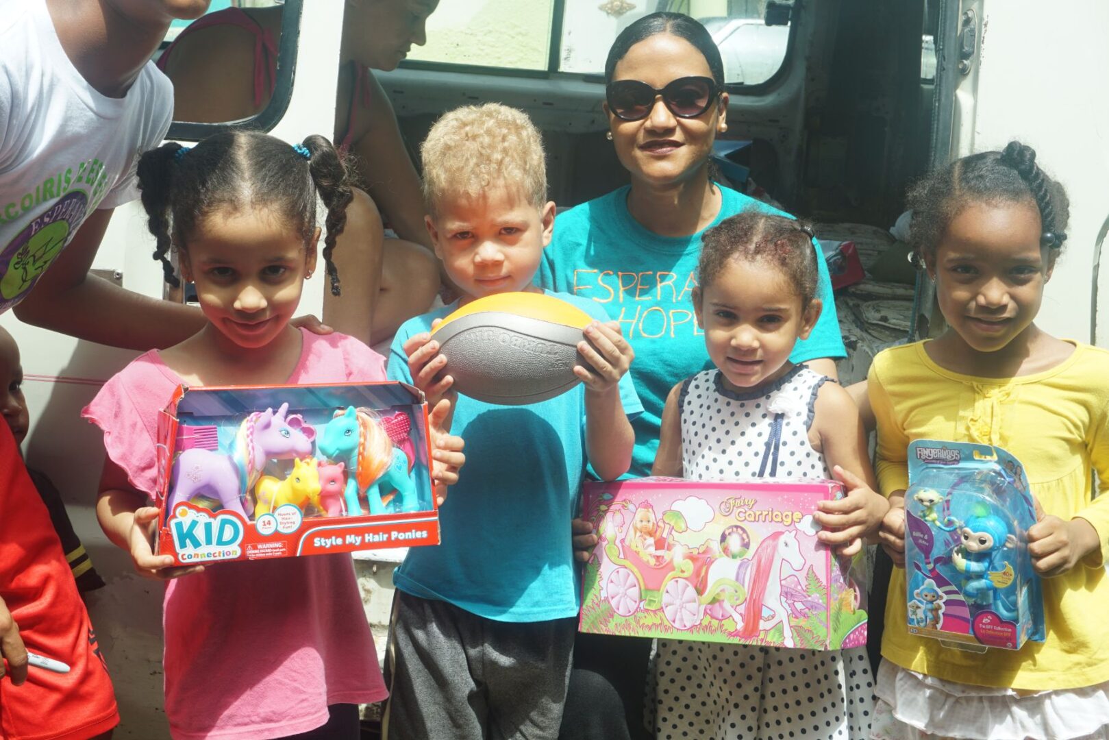 Our staff and four children smiling, showing their toys outside the car