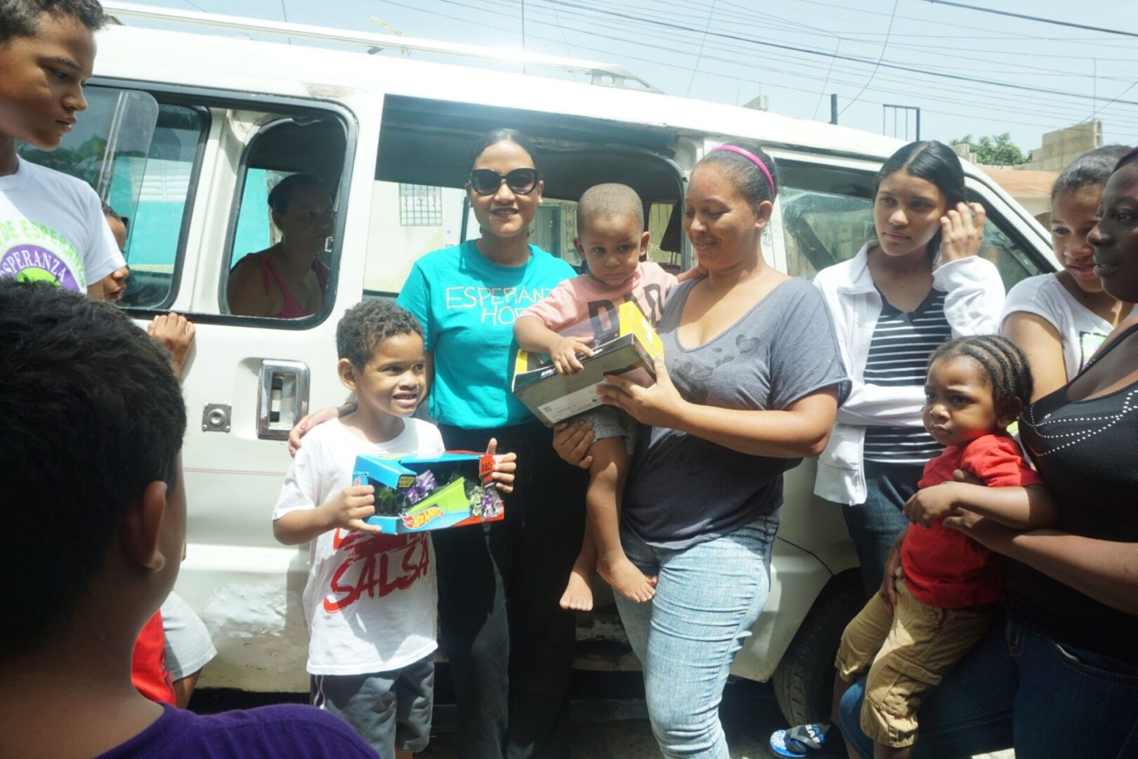 Our staff, a mother carrying a boy, and another boy holding toys outside the car