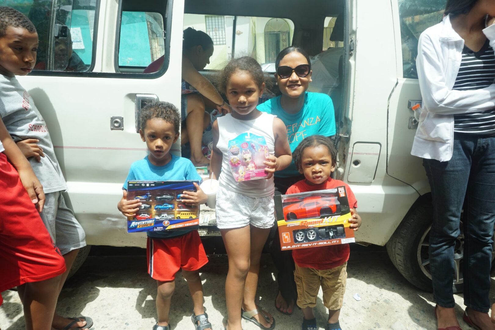 Our staff, a girl, and two boys, the children holding toys outside the car