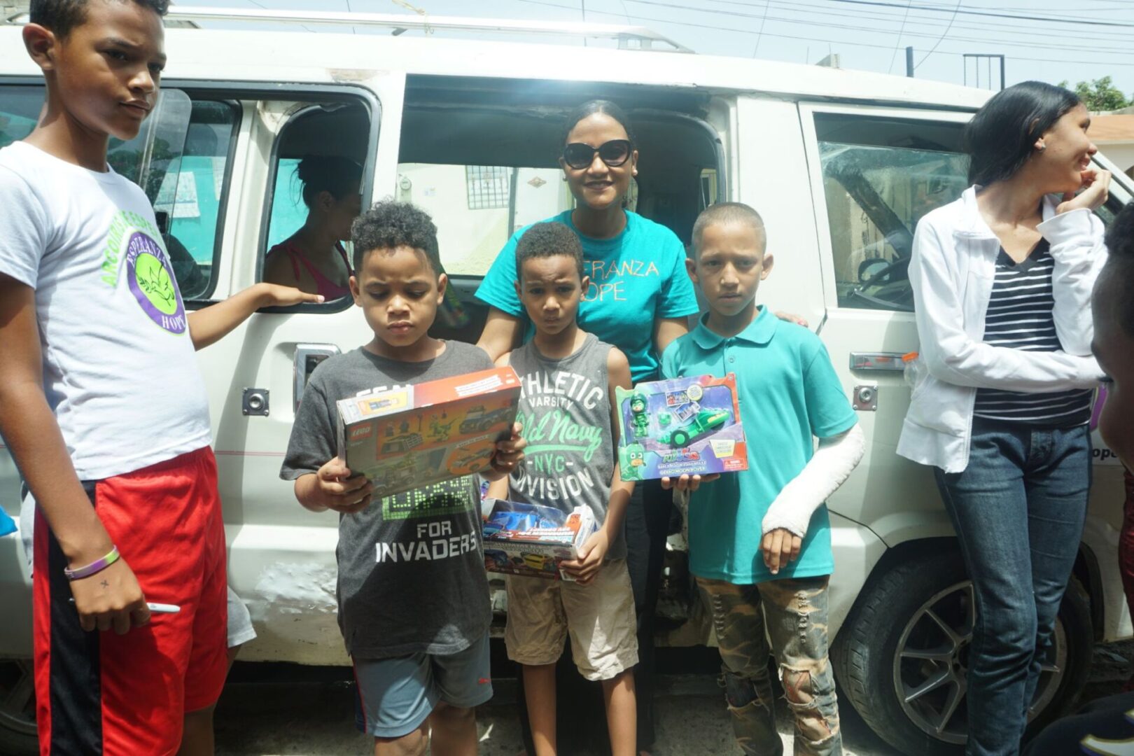A staff and three boys each holding a box of toy outside the car
