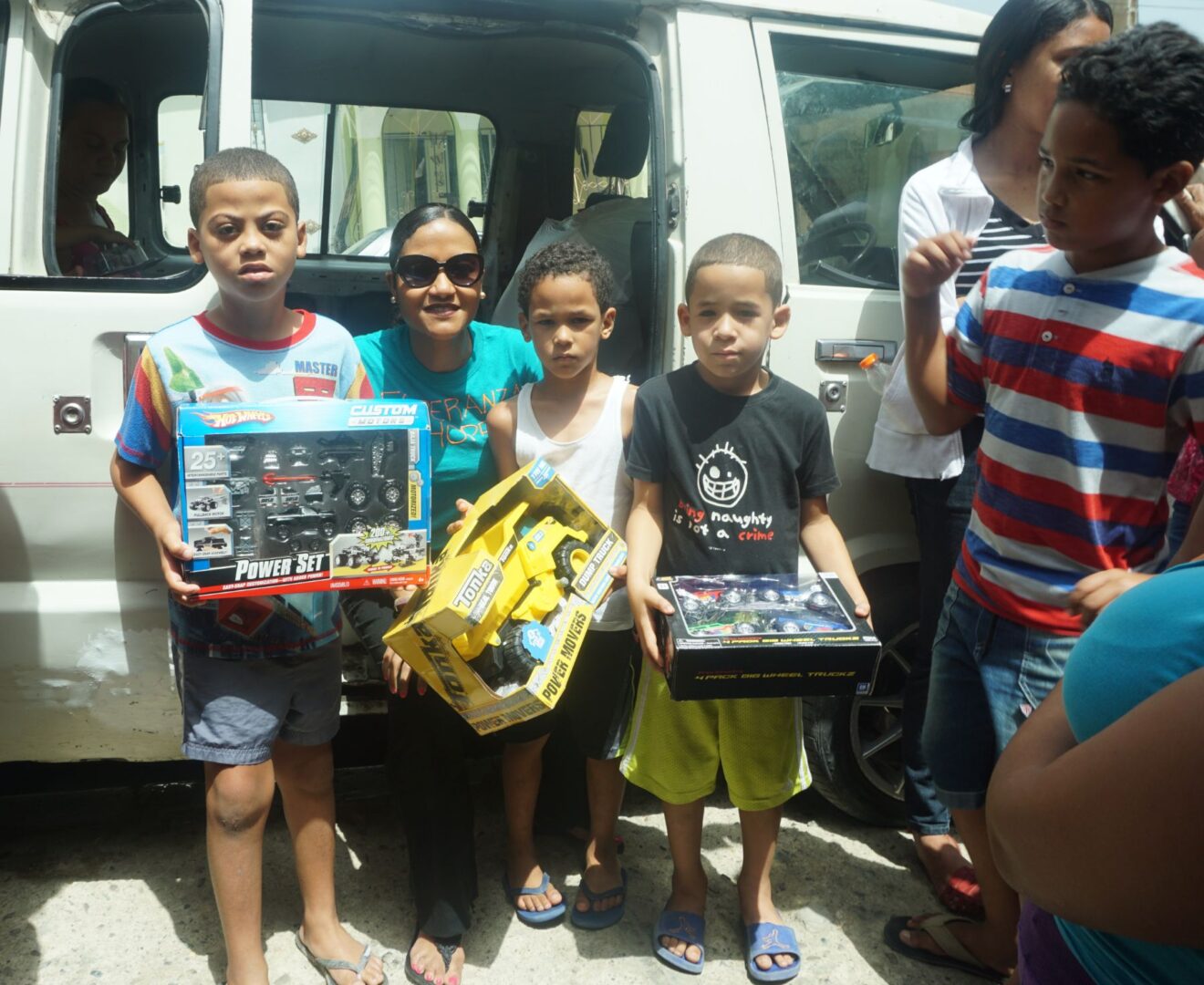 A staff and three boys each holding a box of toy cars outside the car