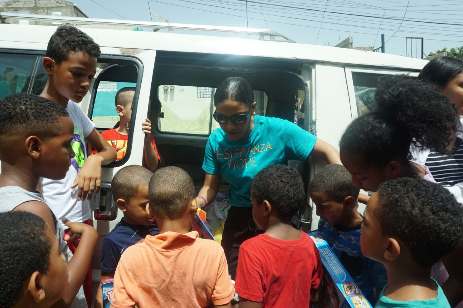 A staff in blue shirt outside the car, crowed by children