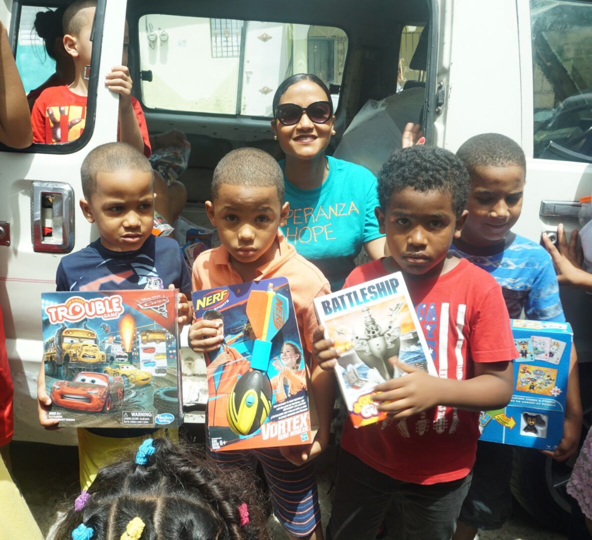 Four little boys holding toys and a staff in blue shirt in front of a vehicle with an opened door