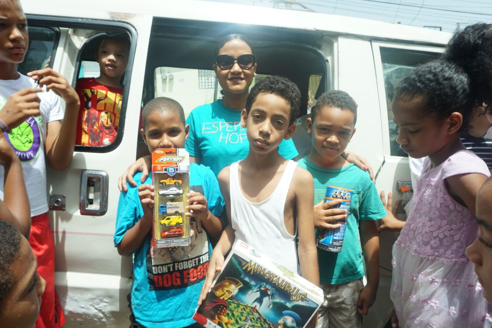 Three boys holding toys and a staff in blue shirt in front of a vehicle with an opened door