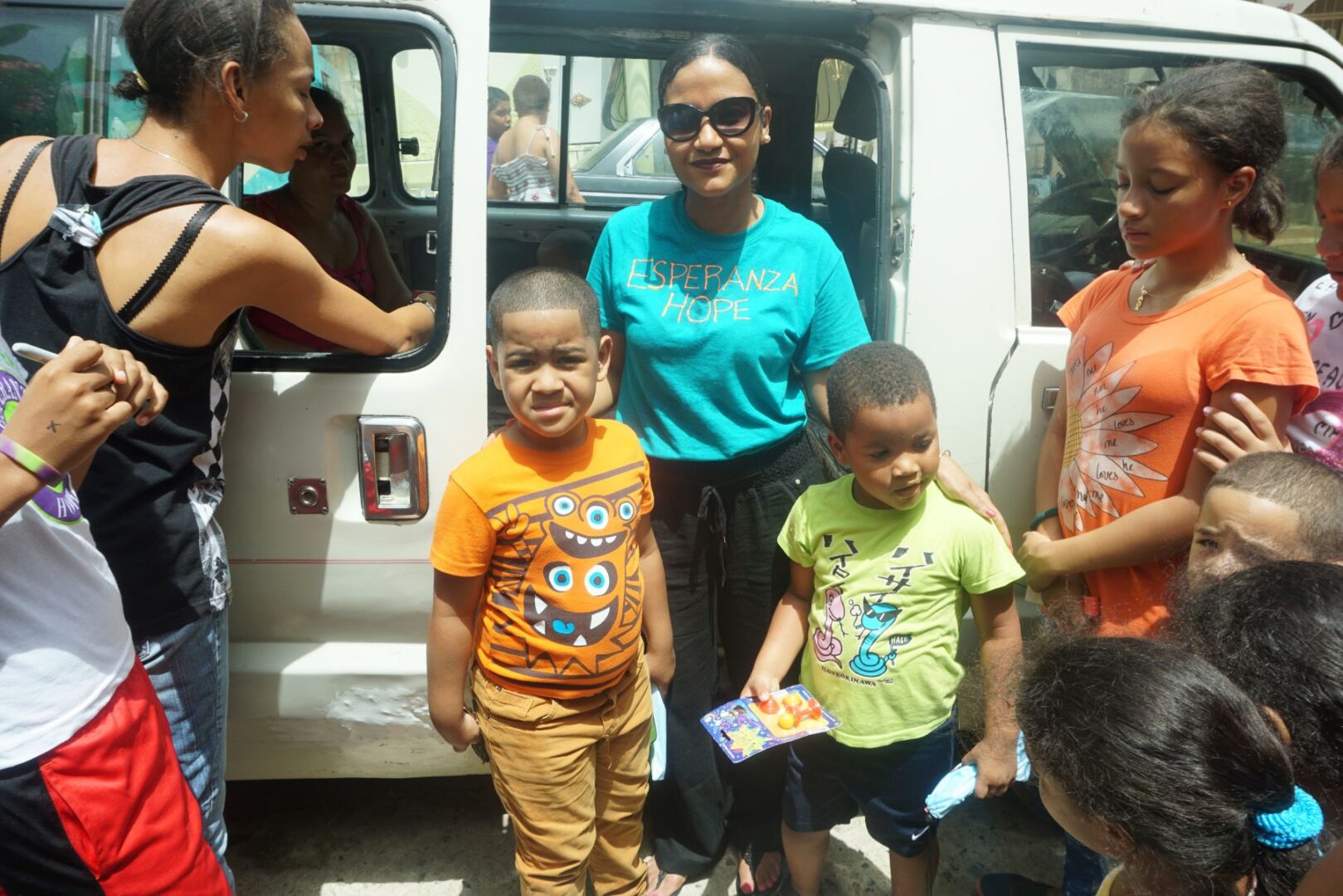 Our staff and two boys holding toys outside the car; children around them
