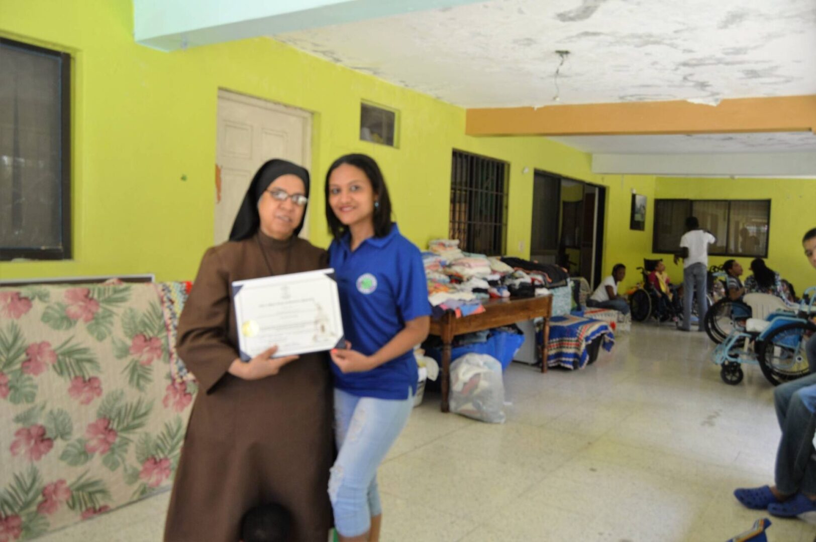 One of our female staff and a nun at Casa Nazaret holding a certificate with the children visible in the background