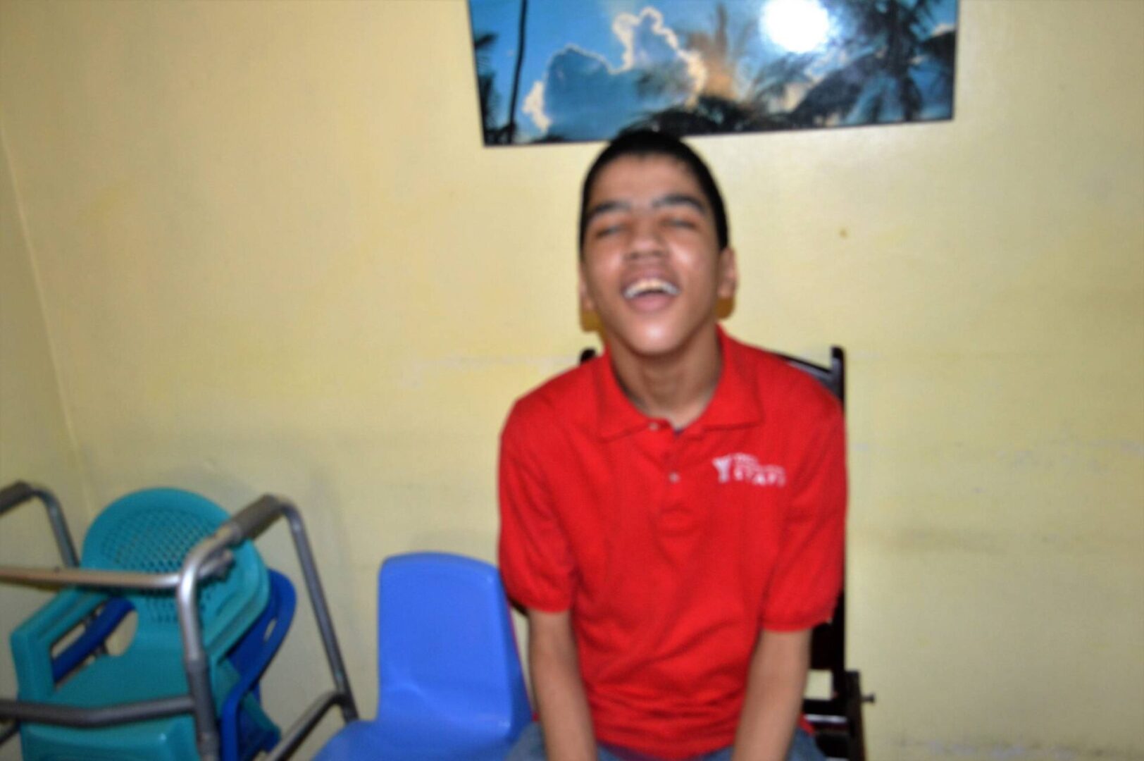 A boy in a red polo shirt sitting on a chair and smiling widely