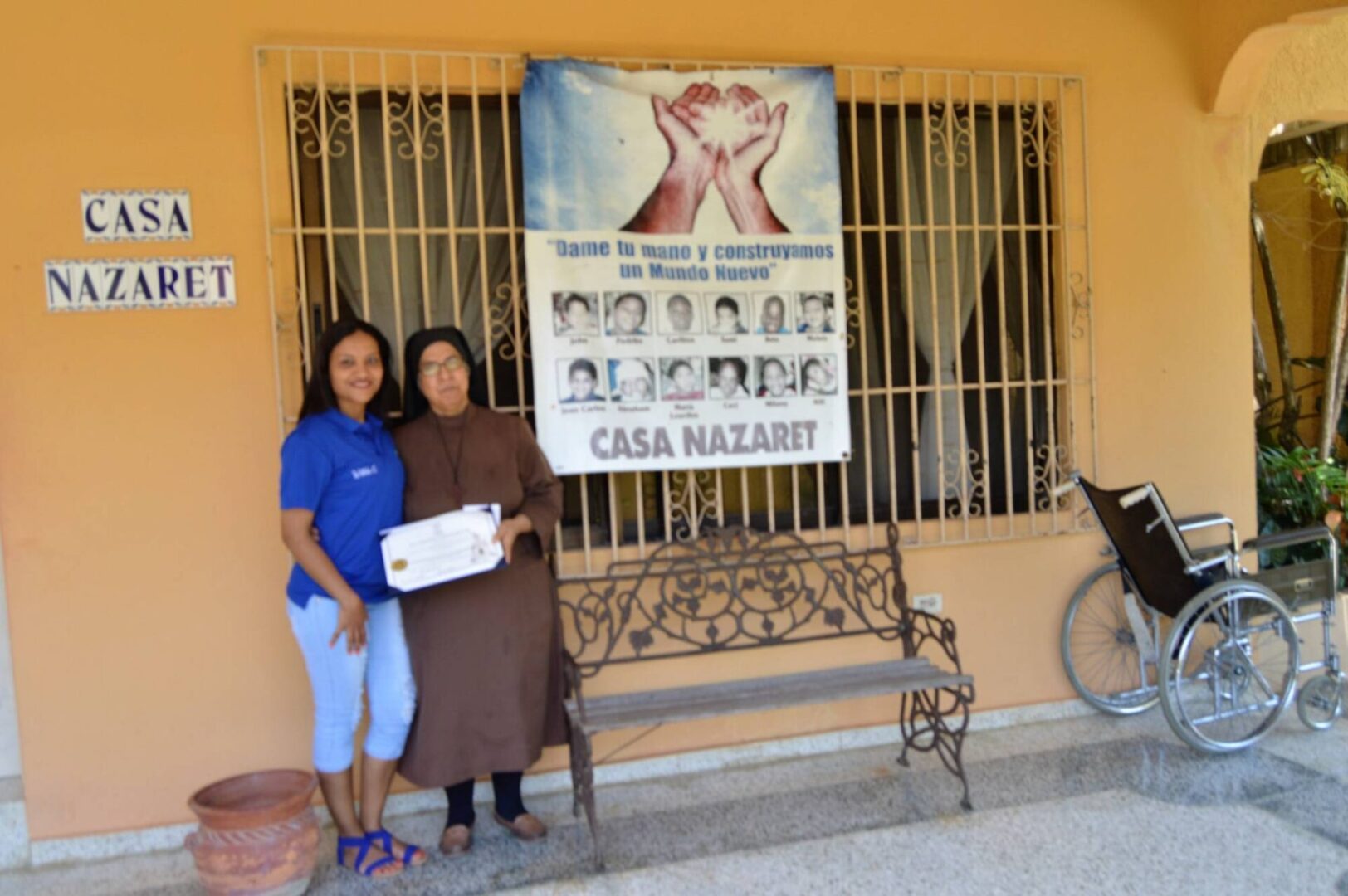 One of our female members and a nun from Casa Nazaret holding a certificate near a Casa Nazaret tarpaulin