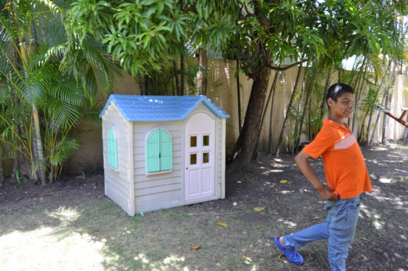 A boy in an orange shirt smiling and walking away from the toy house