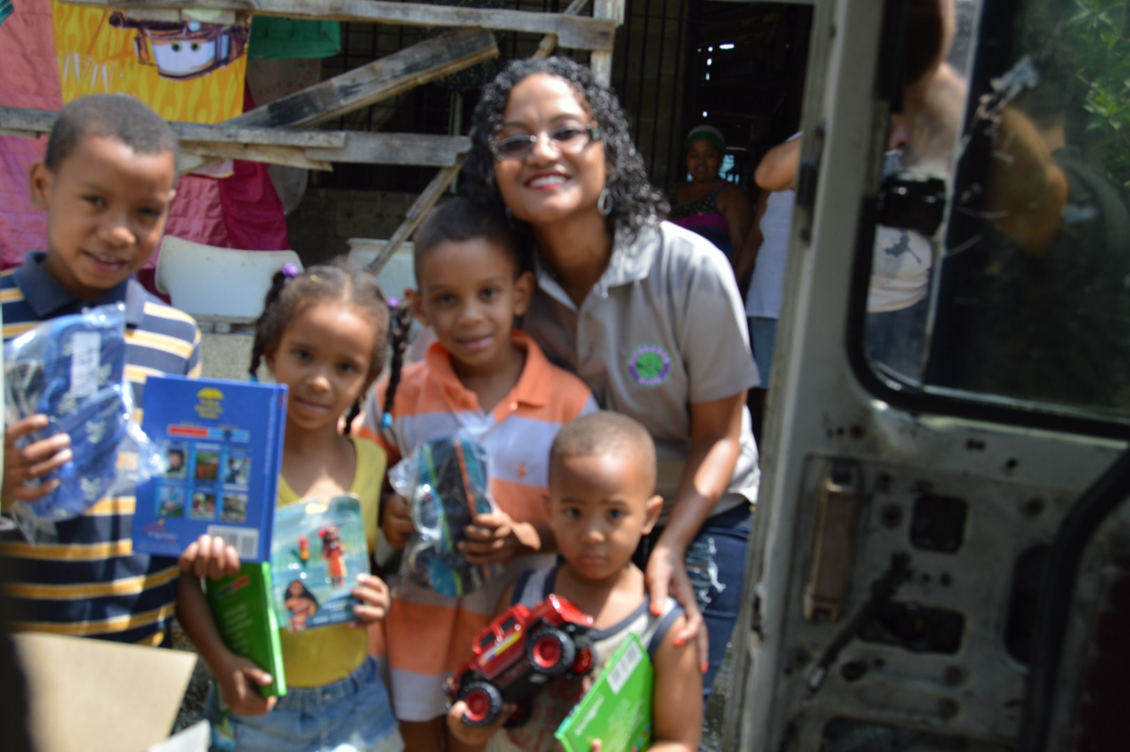 Our staff and the children holding books and toys outside a house
