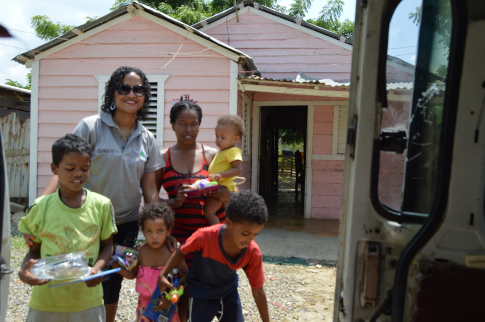 Our staff, a woman carrying a girl, and three children with toys in front of a pink house