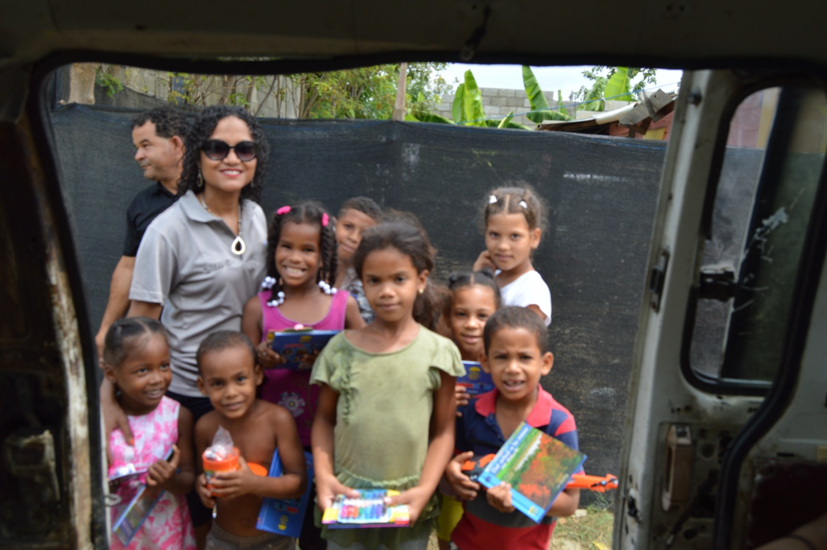 Our staff and a big group of children holding books and toys outside the car