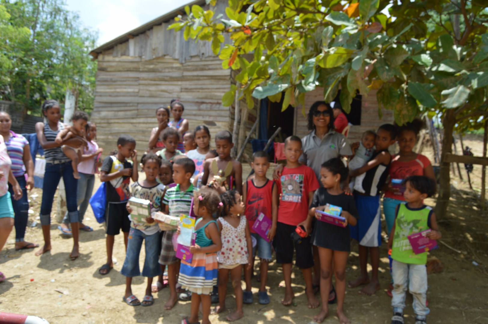 A female staff and a group of children under a tree holding their books and toys