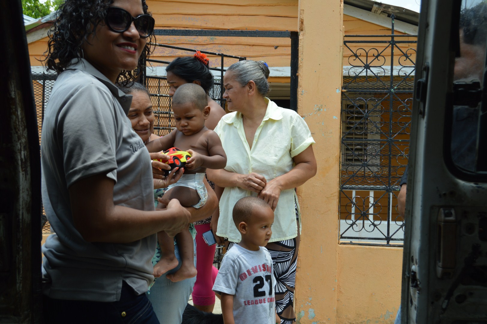 Our staff giving a toy to a child carried by a woman; other women and a child around them