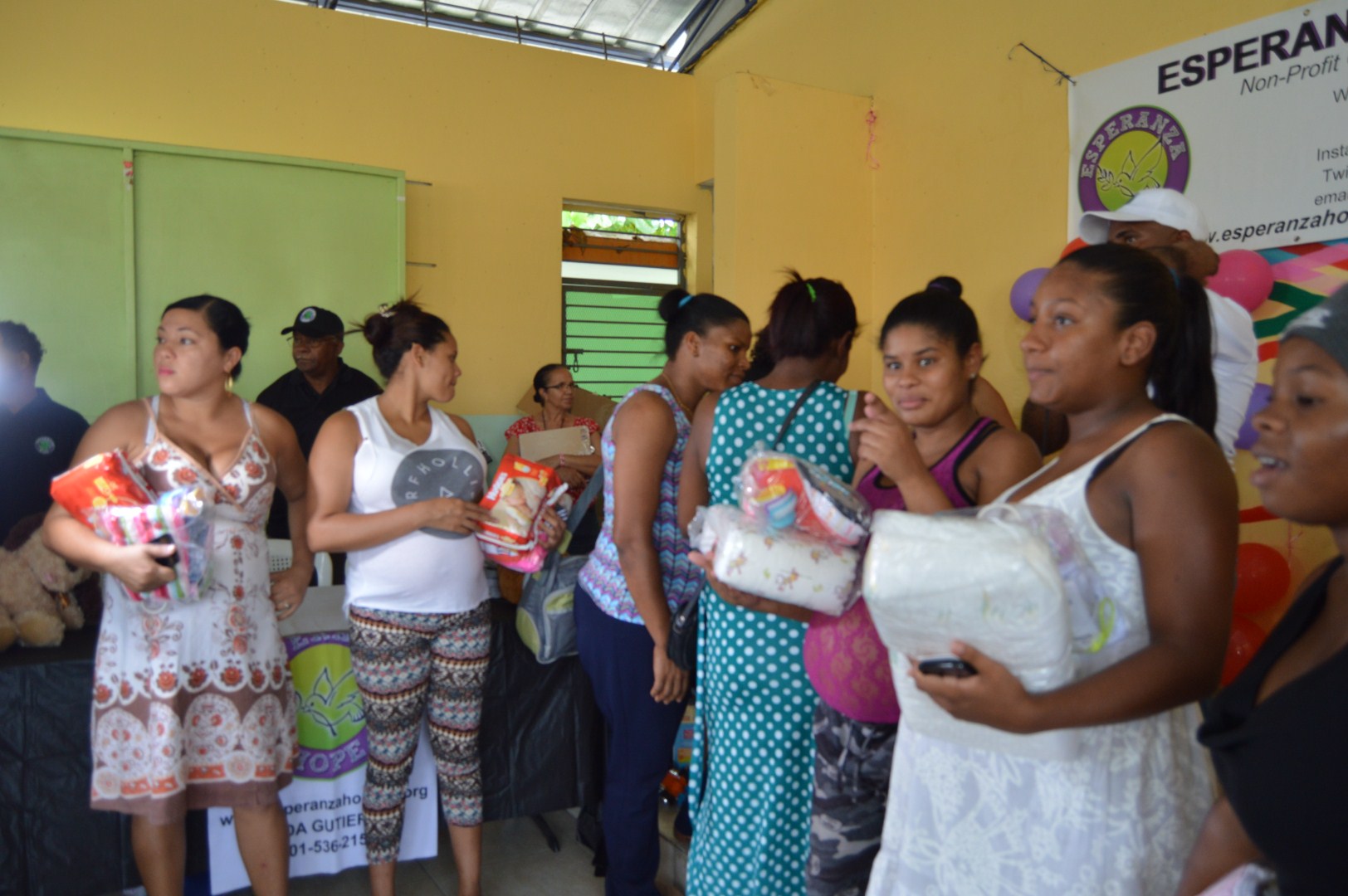 Mothers receiving packs of diapers and clothes, another angle