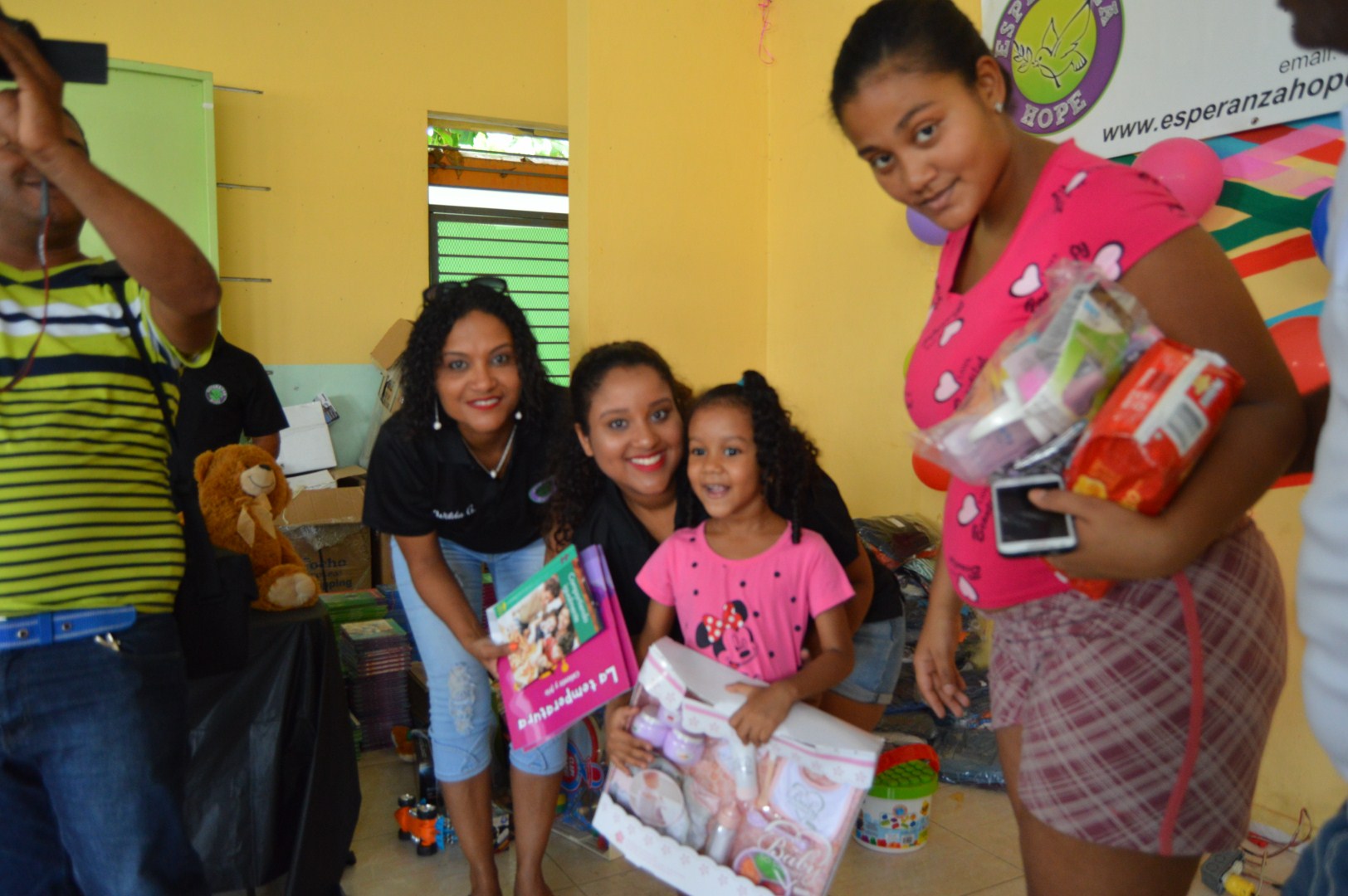 Three women, one holding clothes, and a child holding books and a toy