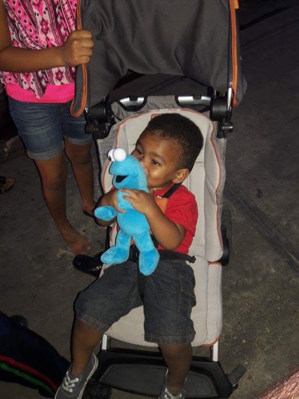 A little boy in a stroller smiling and holding a cookie monster stuffed toy