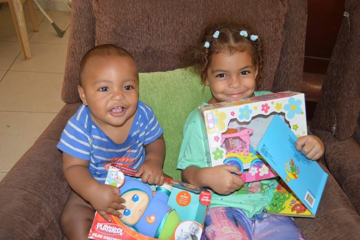 Two young kids smiling and holding toys and books