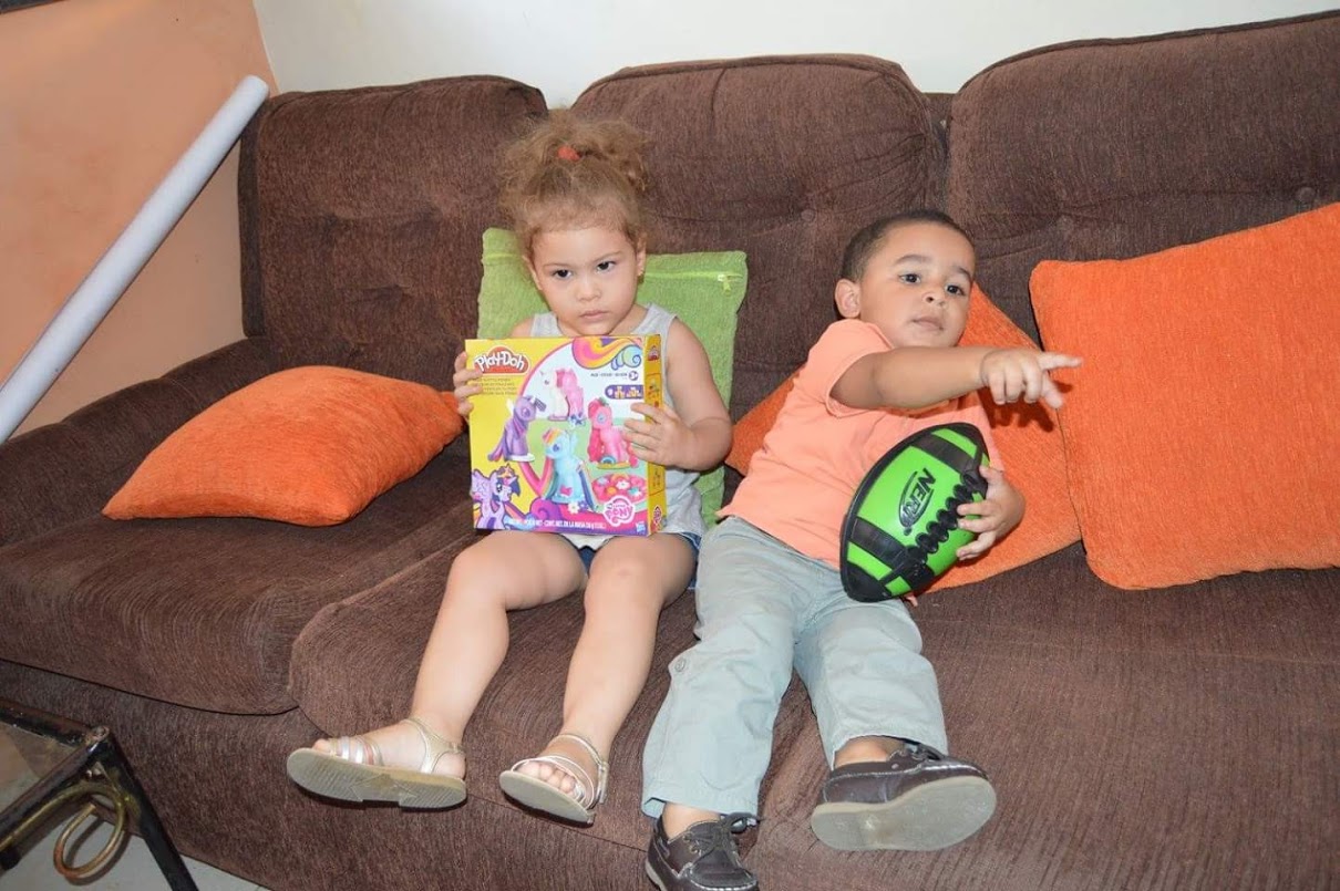 A girl and a boy sitting on a couch, both holding toys
