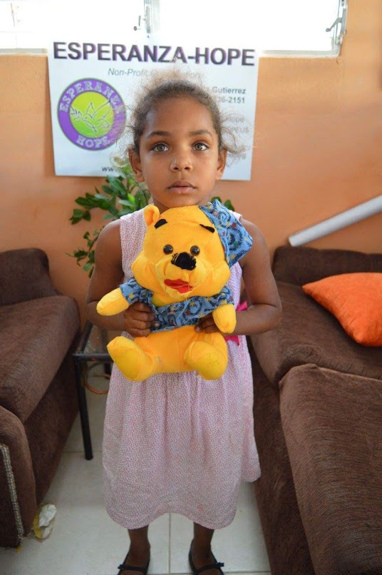 A little girl in a dress holding a Winnie the Pooh stuffed toy