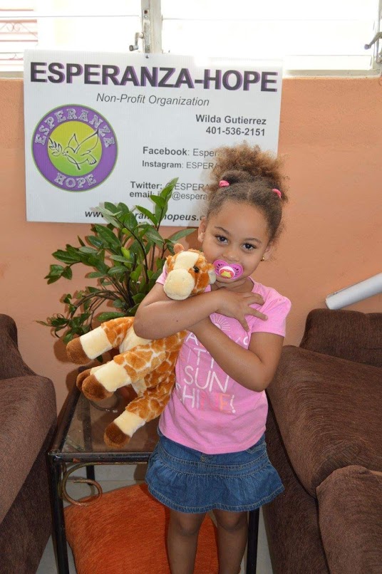 A girl with a pacifier holding a giraffe stuffed toy, smiling