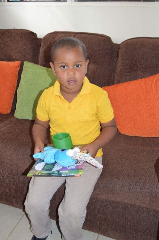 A child in a yellow polo shirt sitting on a couch, holding toys