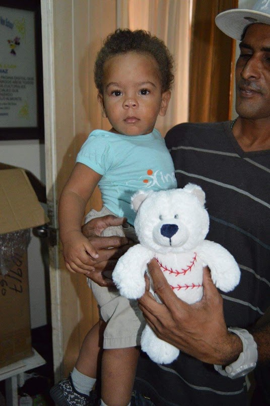 A man carrying a young child and holding a white teddy bear