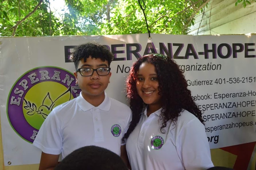 A boy with eyeglasses and a girl and an Esperanza-Hope tarpaulin behind them