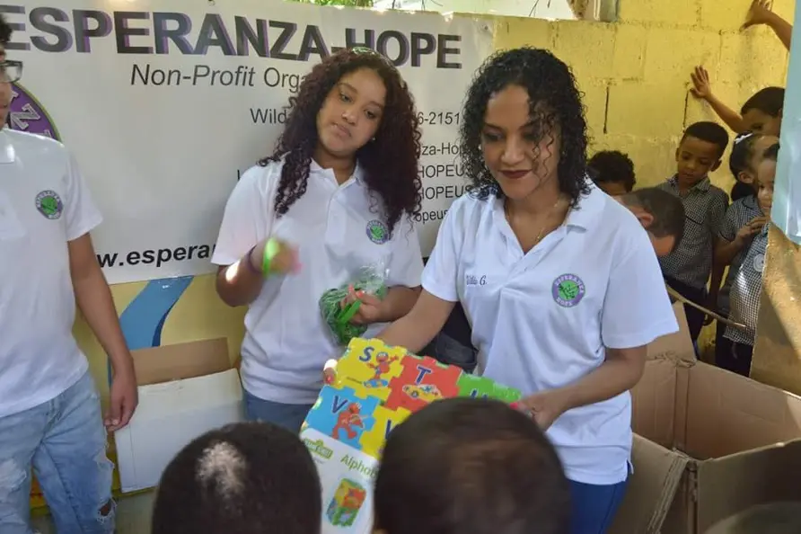 Three staff giving out green wristbands and books to children, 3