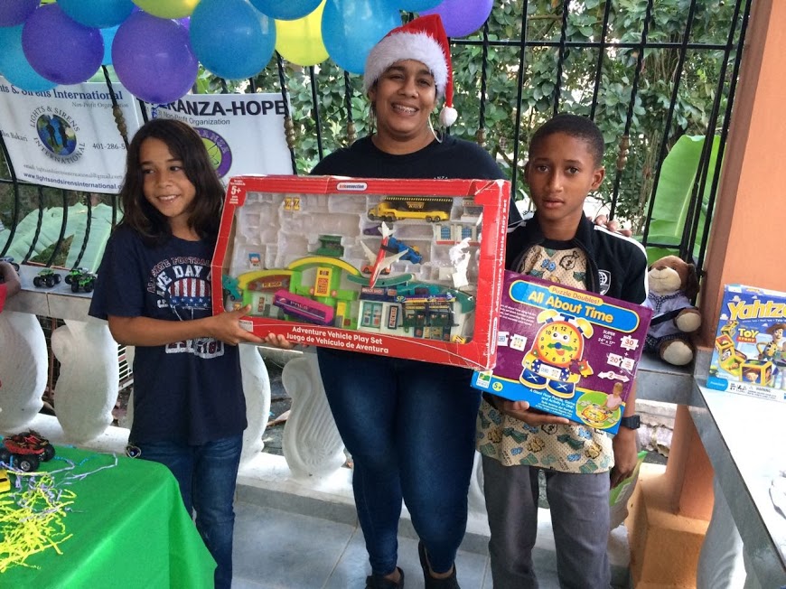 Our staff together with a girl and a boy holding their boxes of toys with the window at the back