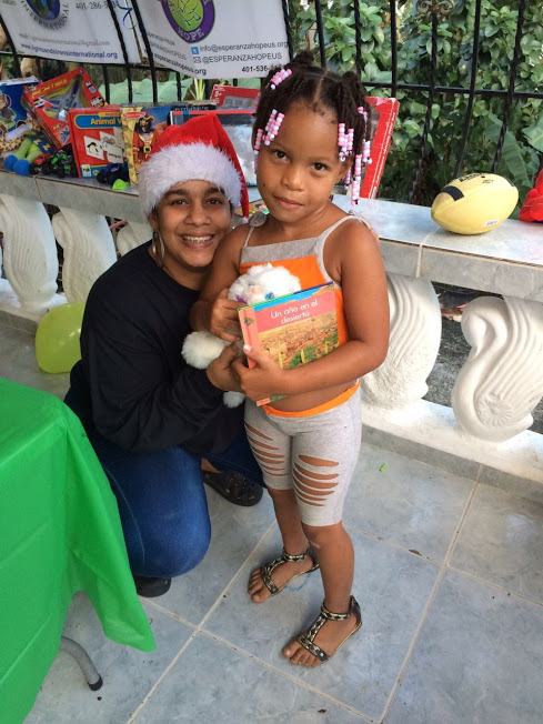 A female staff in Santa hat and a girl holding a book and a stuffed toy, 1