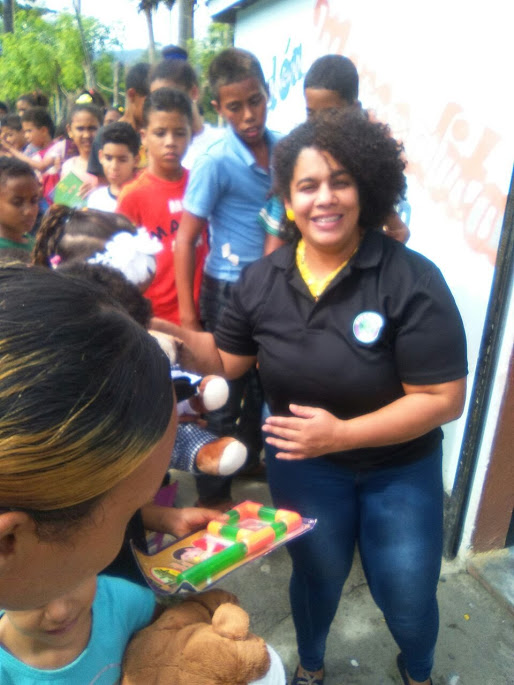 A female staff smiling, giving out a toy to a child